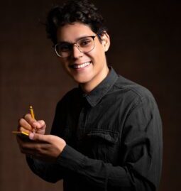 smiling man wearing black denim jacket holding pencil and sticky note while standing